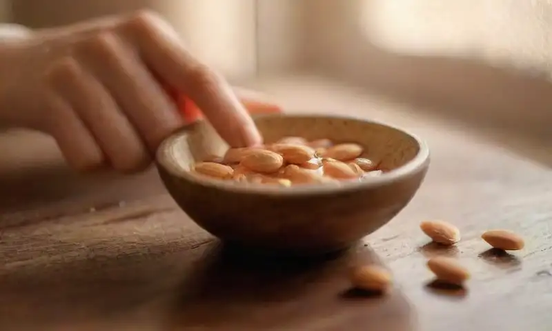 Un espacio cálido y acogedor refleja un momento de autocuidado con aceite de almendra dorado, manos aplicándolo suavemente y un entorno íntimo y sereno