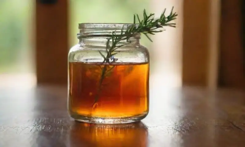 Una botella ámbar suave en una mesa de madera resalta junto a cáscaras de cítricos y romero, creando un ambiente cálido y tranquilo