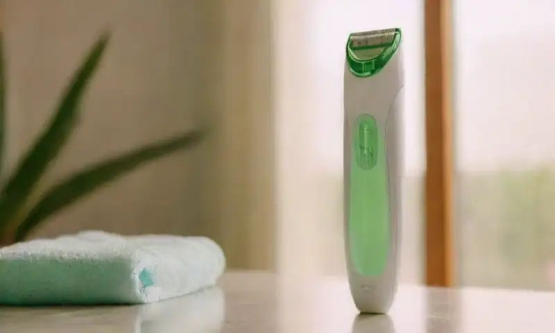 Un dispositivo eléctrico compacto para depilar el vello, con un diseño ergonómico y moderno, colocado sobre una toalla blanca, acompañado de un gel de aloe vera y una planta pequeña