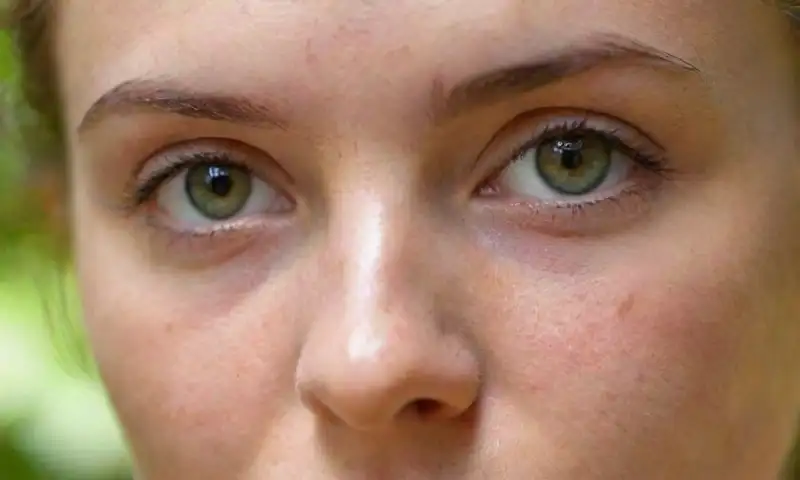 Un primer plano del rostro de un joven con piel suave y defectos sutiles, iluminado por luz natural, que refleja curiosidad y contemplación