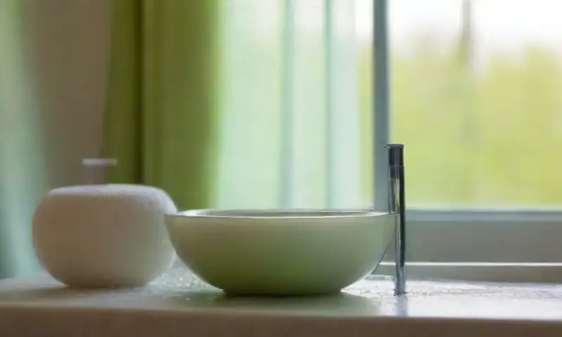 Una escena de baño serena con luz suave, un lavabo de porcelana, toalla blanca, rodillo de jade y elementos que invitan a la tranquilidad y relajación