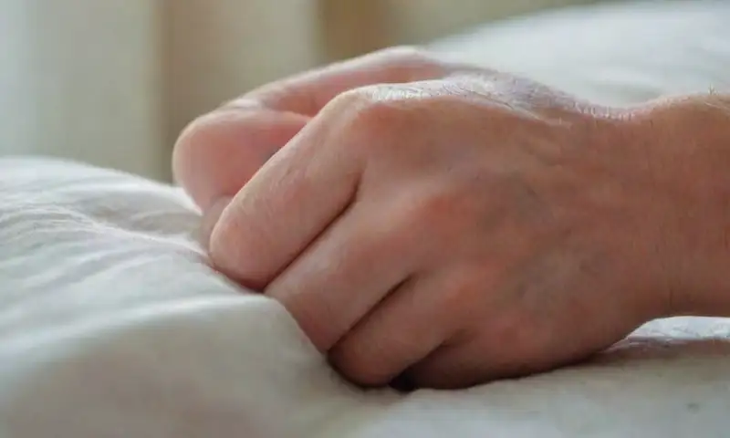 Las manos de un hombre descansan sobre una almohada blanca arrugada
