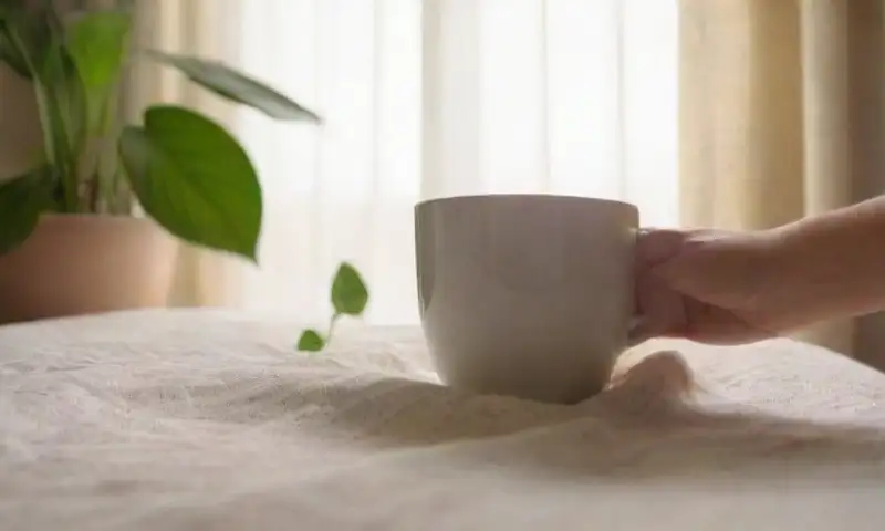 Una escena de dormitorio acogedora con luz suave del amanecer, una mano de mujer sobre las cobijas, una ventana abierta y un ambiente sereno