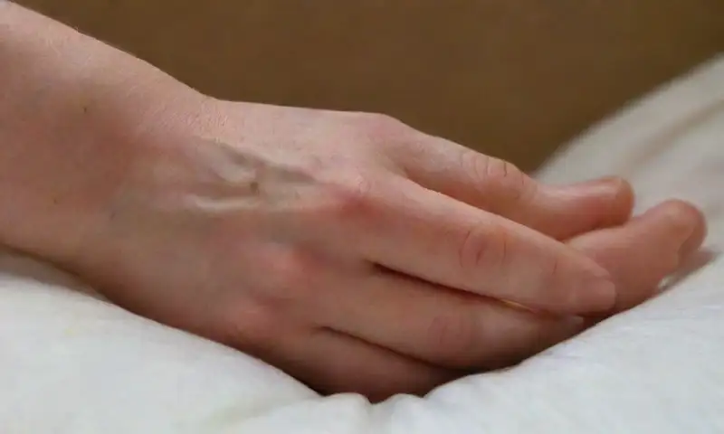Una mano descansa suavemente sobre una almohada blanca, iluminada por la luz natural de la mañana
