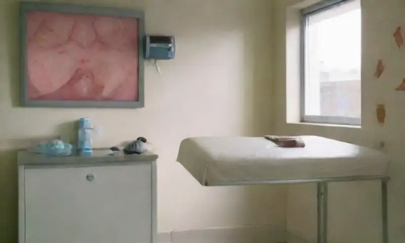 Una sala de examen clínico, limpia y luminosa, equipada con una mesa de acero inoxidable, gráficos anatómicos y herramientas estériles en un ambiente calmado