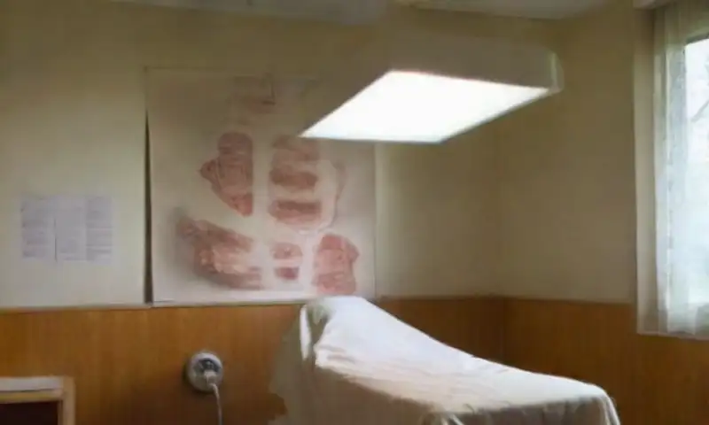Una sala de examen clínica, iluminada y estéril, con una mesa blanca, instrumentos pulidos y un ambiente calmado que refleja precisión anatómica