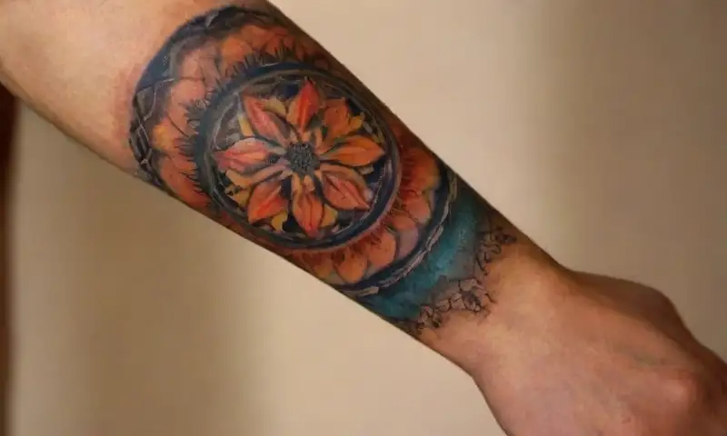 Un primer plano de un antebrazo tatuado con diseños geométricos y florales en colores vibrantes sobre piel bronceada